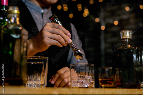 Waitress man standing pours whiskey into a glass 