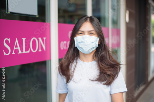 a young woman is getting a haircut in a hair salon , wearing face mask for protection covid-19 , salon safety concept