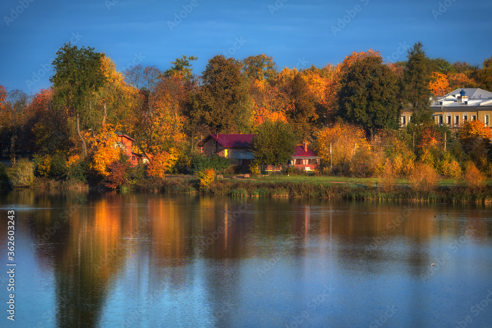 Bright autumn landscape with reflection and houses on the lake.