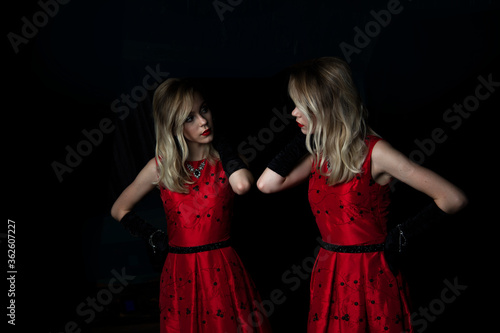 beautiful girl in a red dress and her reflection in the mirror on a black background
