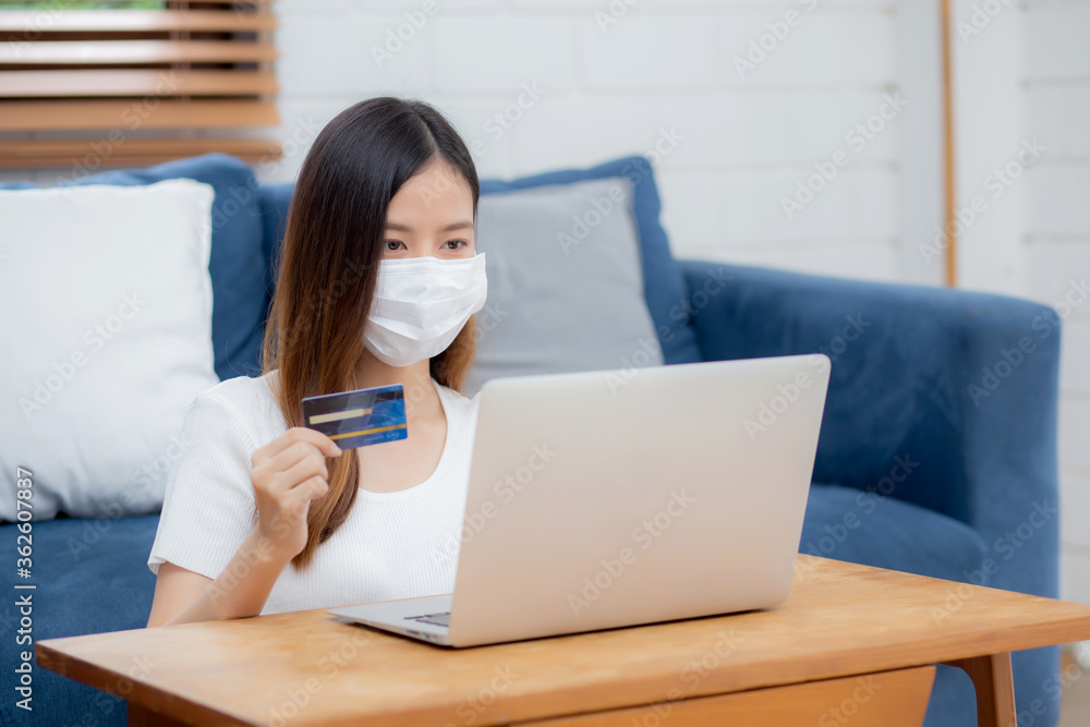 Young asian woman in face mask holding credit card shopping online with laptop computer buy and payment, girl using debit card purchase or transaction of finance, lifestyle and new normal concept. Young asian woman in face mask holding credit card shopping online with laptop computer buy and payment, girl using debit card purchase or transaction of finance, lifestyle and new normal concept.