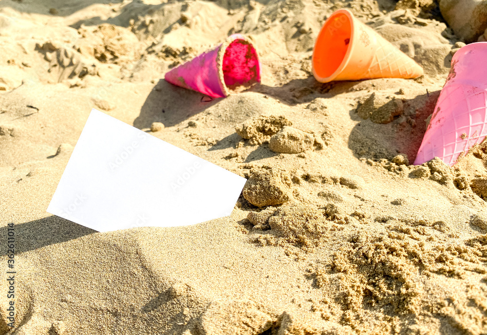 on the sand lies a white business card on the background of toys for children on the sand lies a white business card on the background of toys for children