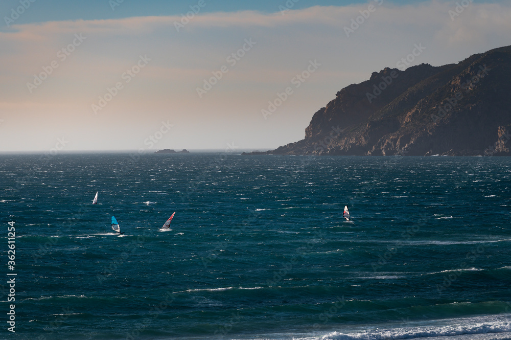 Obraz premium Windsurfers at the Guincho Beach (Praia do Guincho) near Cascais, with the Cabo da Roca on the background, in Portugal