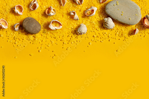 Seashells and stones on a bright yellow sandy background. Summer background with bright sunlight. Travel and vacation concept