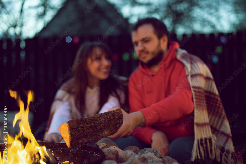 Loving man and woman on romantic party by bonfire, young man adds wood to fire selective focus. Romantic Weekend. Couple In Love Near Camping In Nature. concept togetherness