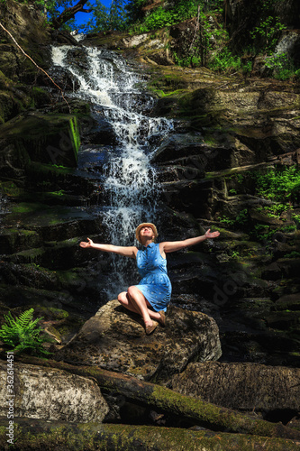 Woman in hat enjoying nature near the forest waterfall.