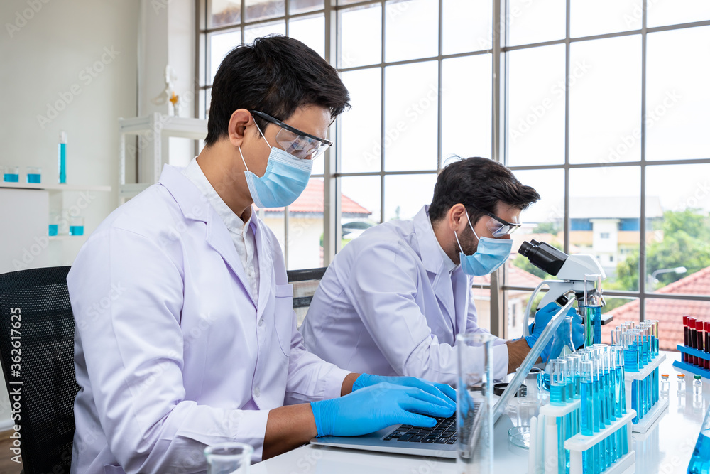 Two male Asian and Arab researcher scientists working in laboratory, conducting study biohazard substance with scientific equipment and microscope Two male Asian and Arab researcher scientists working in laboratory, conducting study biohazard substance with scientific equipment and microscope