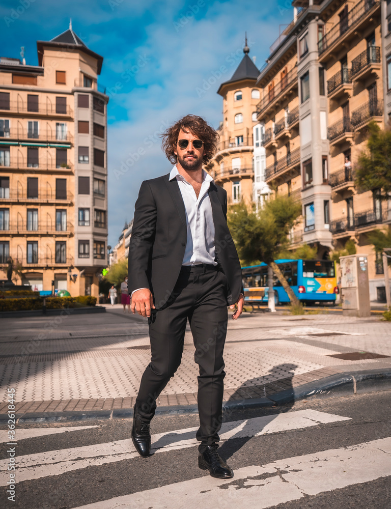 Street style an elegant black suit, white shirt and sunglasses. With a handsome young caucasian man with long hair in the city. Fashion editorial. Crossing a cefras pass in the city Street style an elegant black suit, white shirt and sunglasses. With a handsome young caucasian man with long hair in the city. Fashion editorial. Crossing a cefras pass in the city