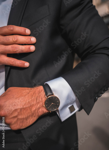 Street style an elegant black suit, white shirt and sunglasses. With a handsome young caucasian man with long hair in the city. Fashion editorial. With a beautiful exclusive watch