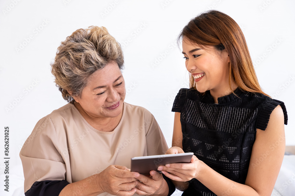 Happy senior elderly Asian woman female mother and daughter enjoy online shopping using digital tablet, looking at camera Happy senior elderly Asian woman female mother and daughter enjoy online shopping using digital tablet, looking at camera