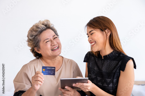 Happy senior elderly Asian woman female mother and daughter enjoy online shopping using digital tablet, looking at camera