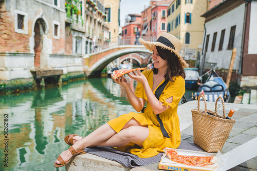 woman sitting on pond with view of venice canal eating pizza © phpetrunina14