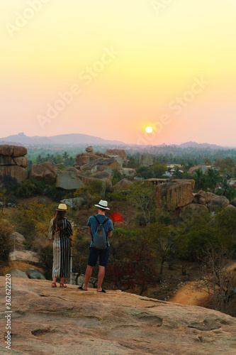 Sunset Point at Hampi. The girl and the guy in hats admire the sunset. Golden evening in India.