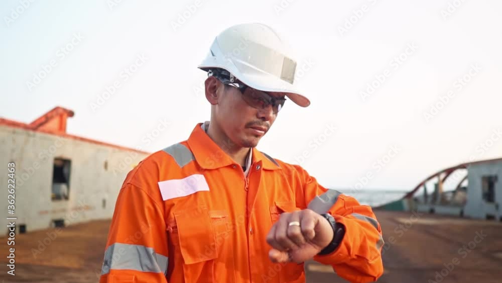 Filipino deck Officer on deck of vessel or ship , wearing PPE personal protective equipment. He checks time Filipino deck Officer on deck of vessel or ship , wearing PPE personal protective equipment. He checks time