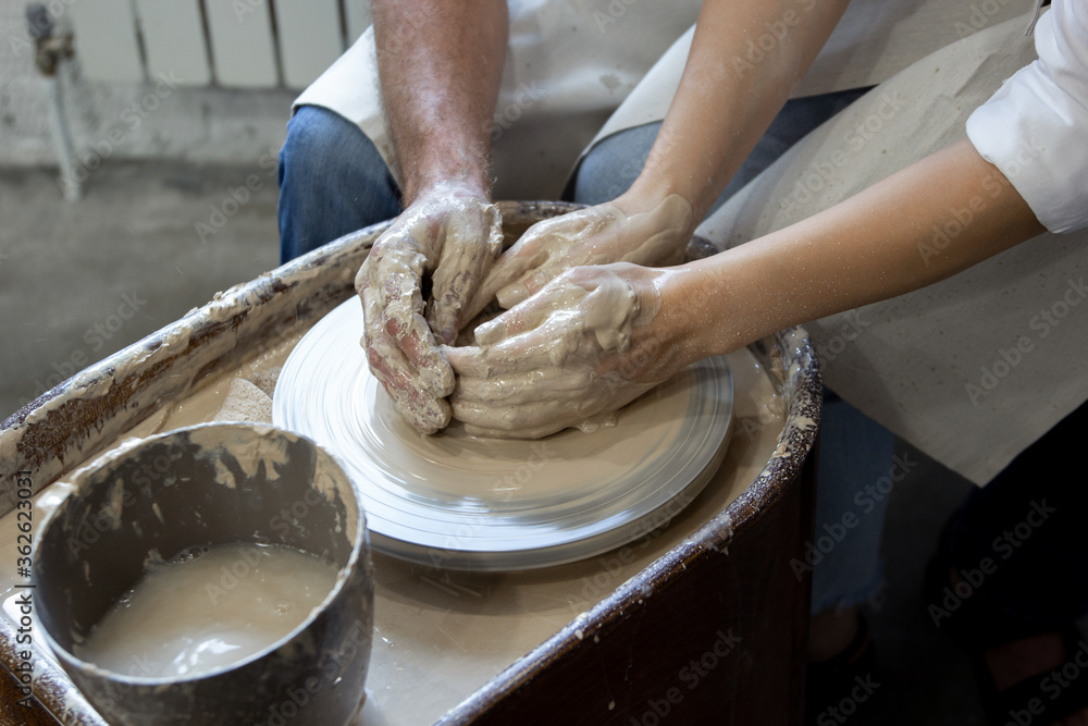 male and female hands in clay behind a potter's wheel
