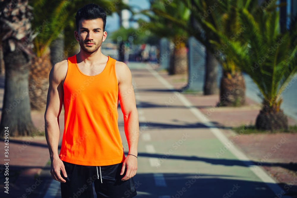 Half length portrait of muscular build handsome male posing for the camera outdoors, handsome runner in bright t-shirt resting after workout, copy space area for your text message or advertise content