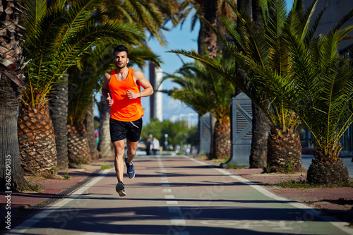 Full length portrait of handsome male runner jogging fast in tropic urban setting, muscular build man working out outdoors at sunny afternoon with copy space area for text message or advertise content © BullRun