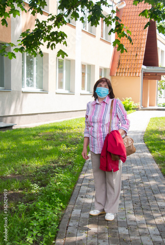 Elderly old woman with a medical mask on her face stands on a deserted street