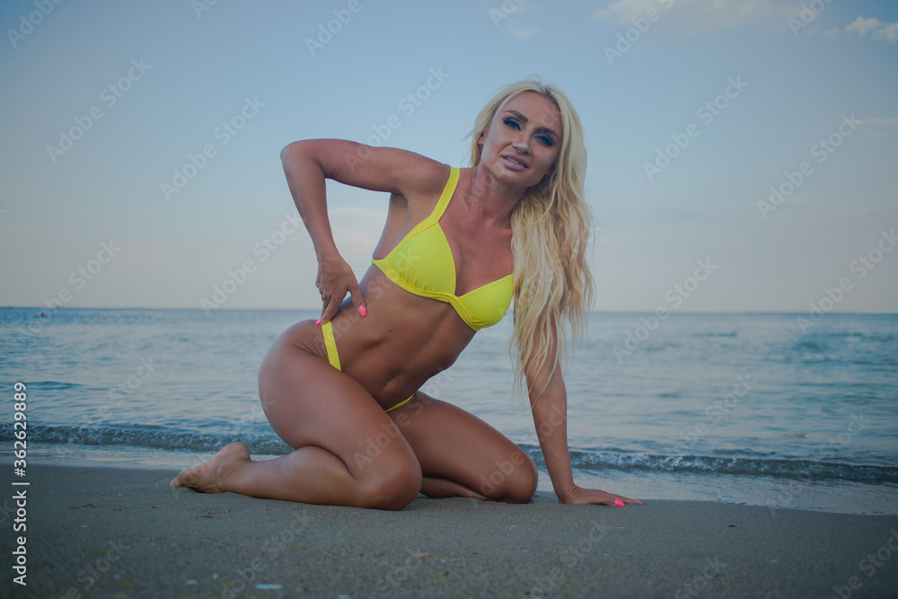 Fototapeta premium tanned blonde in a yellow bathing suit on the seashore at sunset 