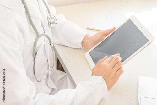 Online visit to doctor. doctor in white coat looks at tablet  sitting at table  free space
