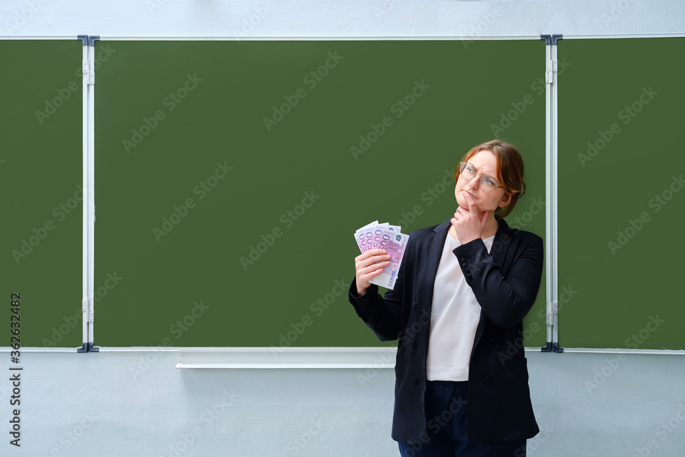 The student thought about the money for studying at the university. A teacher in a school class holds in his hand the money in euros. Place under the text on the blackboard, copy space. The student thought about the money for studying at the university. A teacher in a school class holds in his hand the money in euros. Place under the text on the blackboard, copy space.