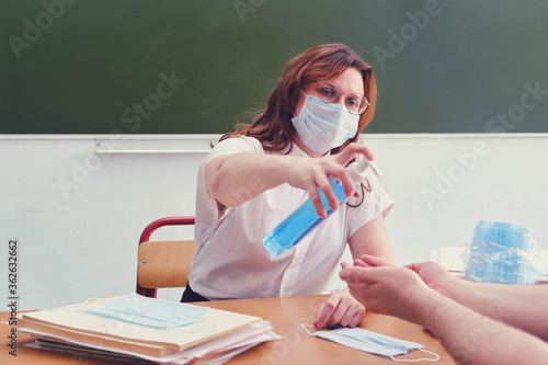 Woman school doctor treats his hands with antiseptic. Teacher in medical mask uses hand sanitizer, copy space. Classroom safety concept during lessons in the flu virus pandemic