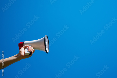 Megaphone in a female hand on a blue background. No people. Cropped photo. A woman holds a sound amplifier against the sky.