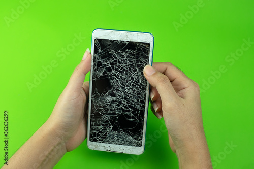 Hand holding smartphone screen is cracked on green background