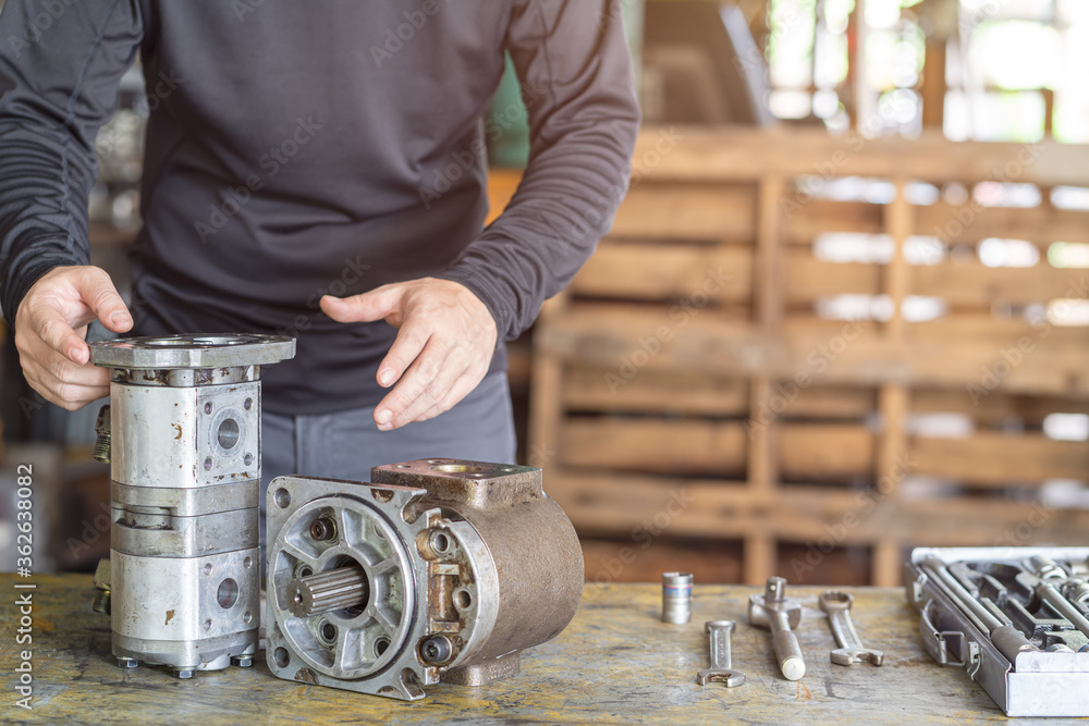 Professional mechanic man inspection hydraulic gear pump of wheel loader in workshop, repair maintenance heavy machinery