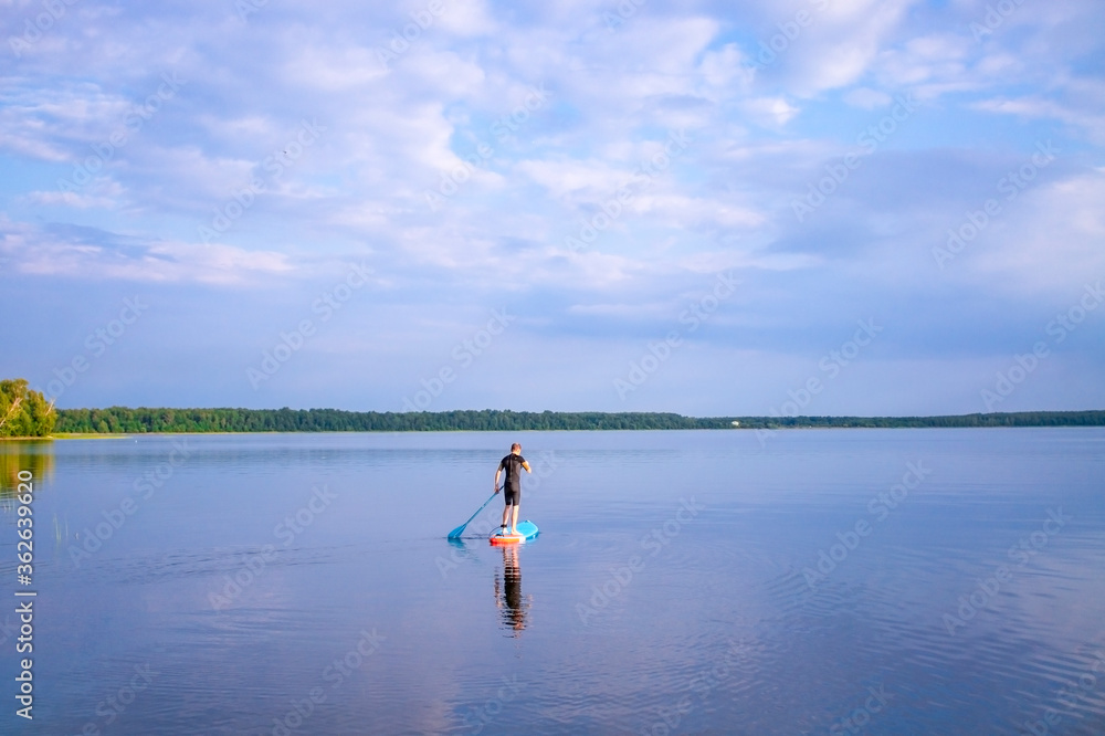 Man is paddling on a sup board on the lake. selective focus. Paddle board stand up. Lake landscape and blue cloudy sky. Man is paddling on a sup board on the lake. selective focus. Paddle board stand up. Lake landscape and blue cloudy sky.