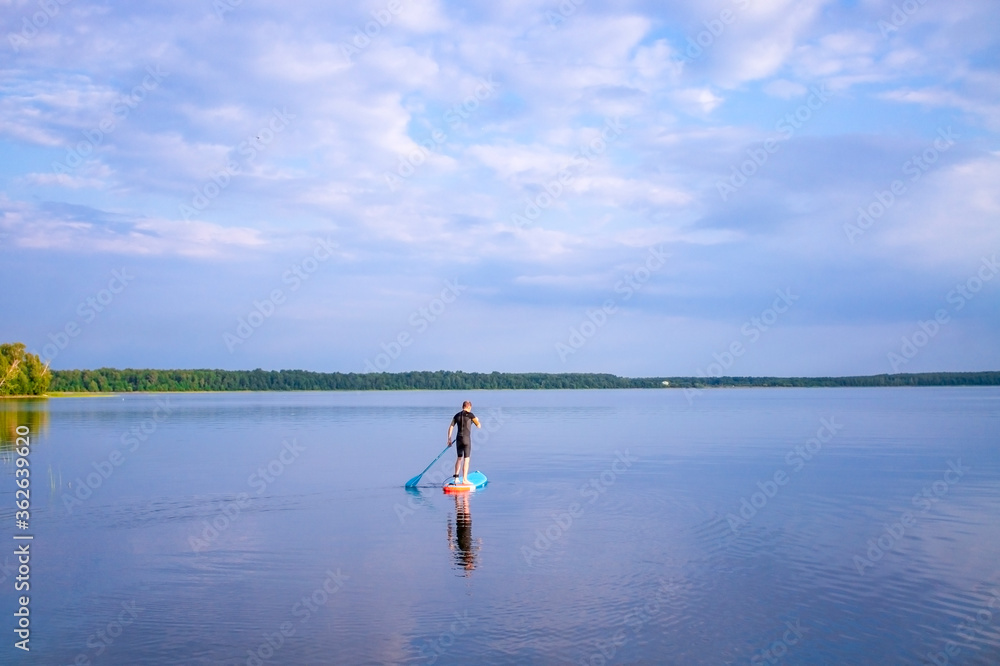 Man is paddling on a sup board on the lake. selective focus. Paddle board stand up. Lake landscape and blue cloudy sky.