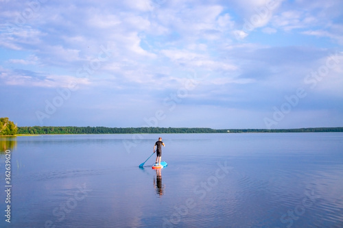 Man is paddling on a sup board on the lake. selective focus. Paddle board stand up. Lake landscape and blue cloudy sky.