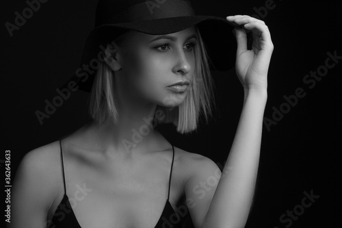 Black and white portrait blondes on a black background in a hat and Tank Top With Thin Straps. holding the brim of his hat with his hands © Roman Kornev