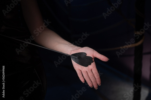 An unrecognizable woman demonstrates an elegant thin leather strip whip in a dark bedroom. Close-up of female hands with a bdsm toy. Pain and pleasure.Adult toy for slaps.