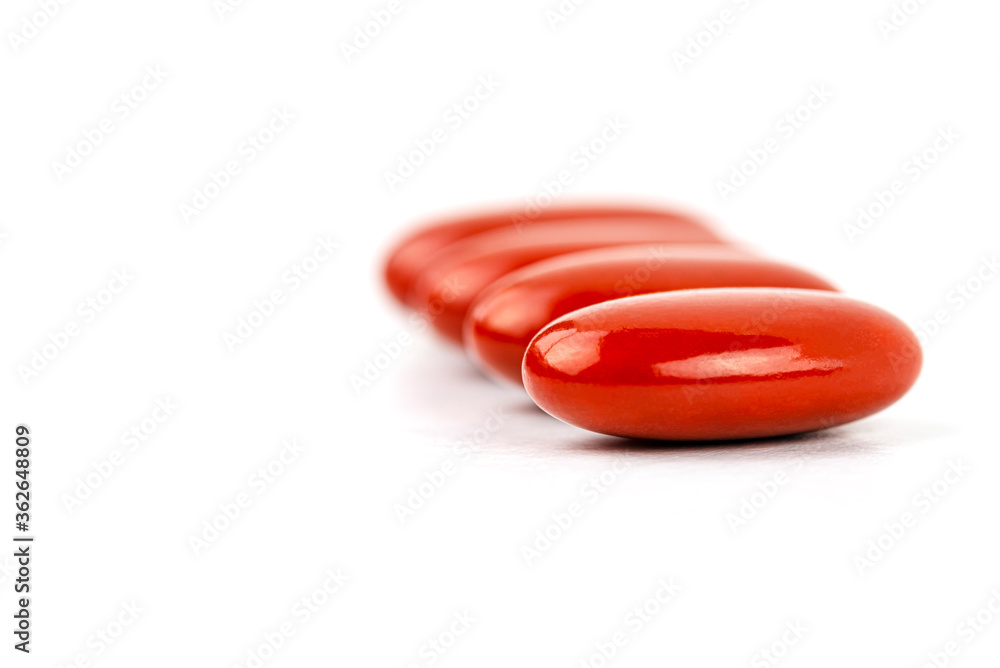 A macro shot of four red film-coated tablets arranged in a row, isolated on a white background. A macro shot of four red film-coated tablets arranged in a row, isolated on a white background.