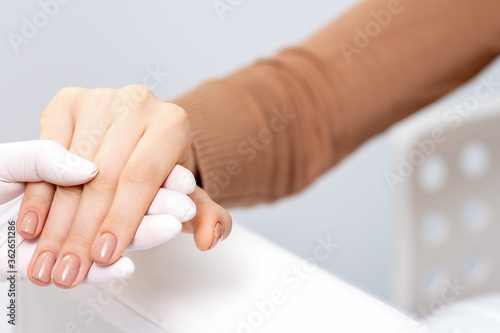Close up of human hand in protective glove holding female fingers with beige manicure in beauty salon
