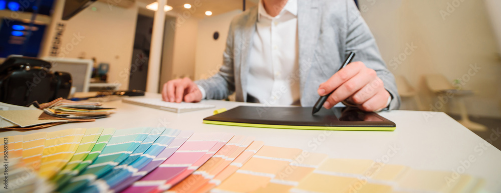 Photographer-designer works at a table, holds a stylus of a graphic tablet in the river Photographer-designer works at a table, holds a stylus of a graphic tablet in the river