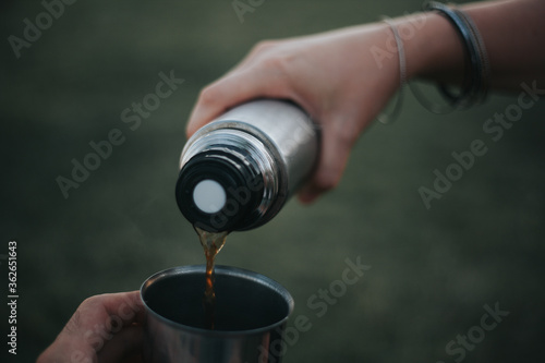 Drinking filter coffee in the park. Pouring coffee into the cup from the thermos with green background with no people. Coffee love concept. Camping concept.
