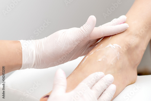 Human hands in protective gloves doing foot massage with moisturizing or peeling cream in eauty salon