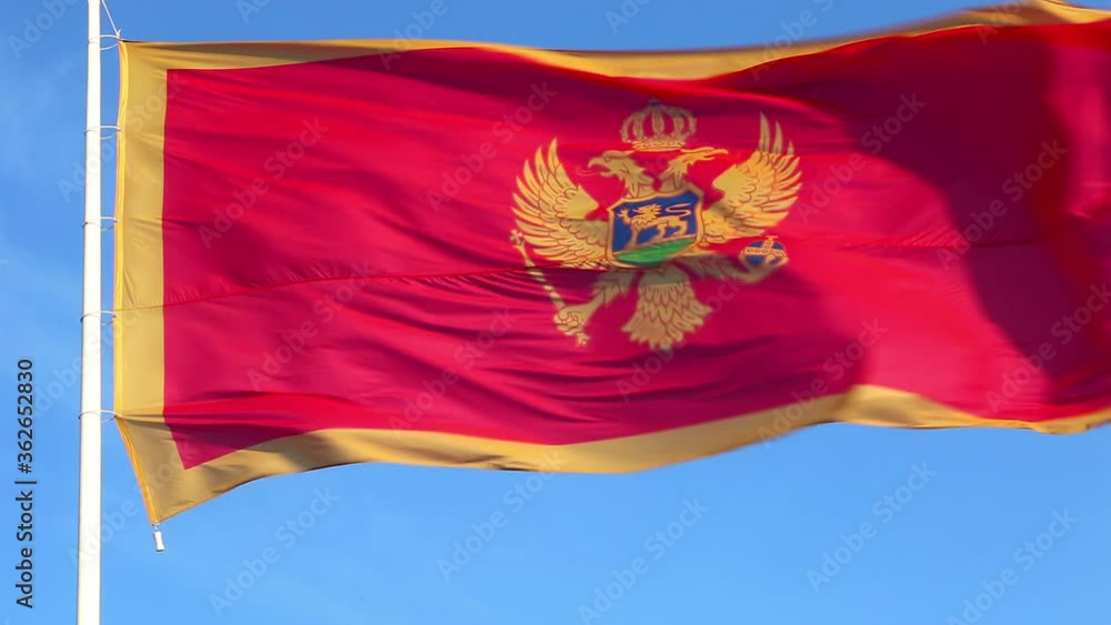 Waving national flag of Montenegro on a pole - red and yellow against clear blue sky on a sunny day. Slow motion. Waving national flag of Montenegro on a pole - red and yellow against clear blue sky on a sunny day. Slow motion.