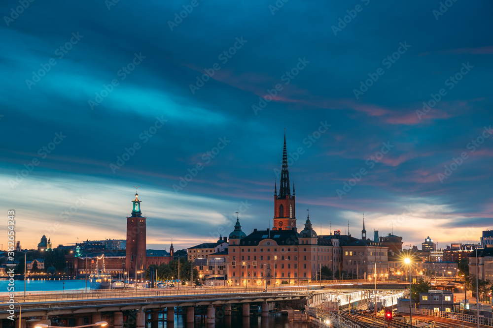 Fototapeta Stockholm, Sweden. Scenic View Of Stockholm Skyline At Summer Evening Night. Famous Popular Destination Scenic Place Under Dramatic Sky In Night Lights. Riddarholm Church, City Hall, Subway Railway