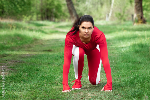 A girl in a tracksuit is preparing to run, physical exercises against the backdrop of nature, prelaunch pose. The concept of a healthy lifestyle, exercise, fresh air. Copy space. photo