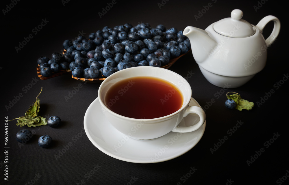 Still life, cup with tea, teapot, blueberry and dry leaves of mellisa on dark background Still life, cup with tea, teapot, blueberry and dry leaves of mellisa on dark background