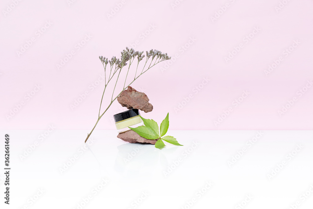 Obraz premium Cosmetic jar with yellow butter or cream with natural volcano stones and flower on white and pink background. High quality photo