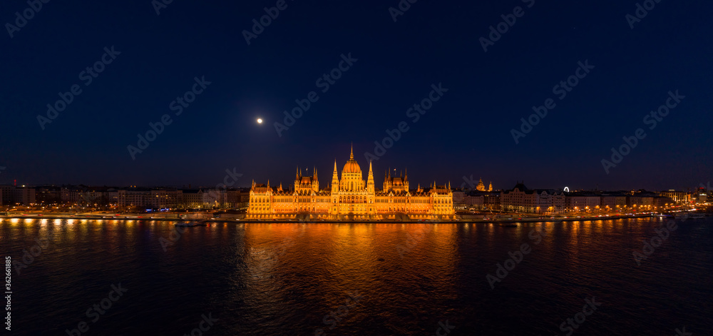 Panoramic aerial drone shot of front facade of Hungarian Parliament with lights on in Budapest night
