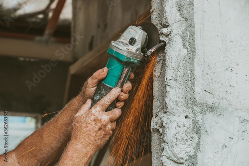 An elder man's hands grip an electric cut off tool igniting sparks photo