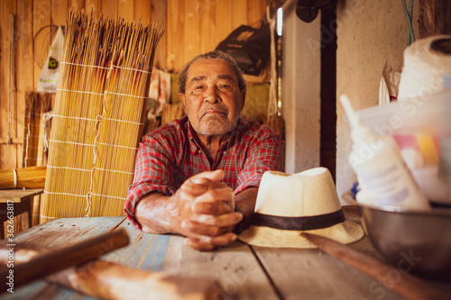 Old artisan in a local community of Garopaba, Brazil. Craftsman resting at his wooden workshop. Elder wearing red plaid shirt photo