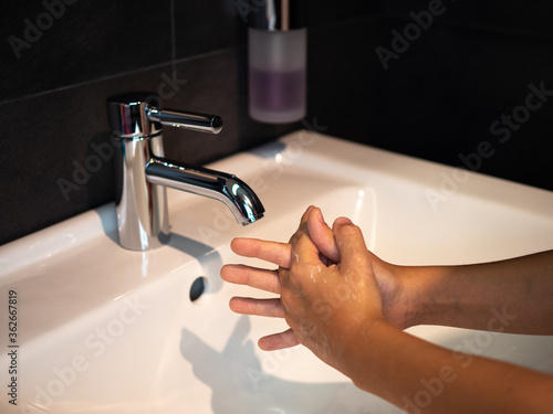 Fototapeta Naklejka Na Ścianę i Meble -  Hand washing personal hygiene boy washing hands rubbing soap for 20 seconds following steps, cleaning wrists and rinsing under water at home bathroom. COVID-19 infection prevention handwashing.
