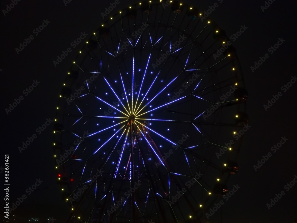 Night photo high modern ferris wheel with a bright pattern of blue and yellow lights glowing in the dark