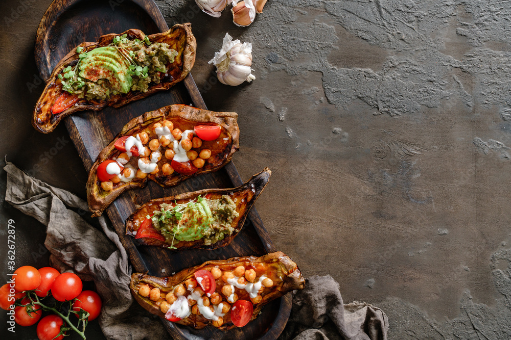 Baked sweet potato toasts with roasted chickpeas, tomatoes, goat cheese, avocado and spices on wooden board over brown background. Healthy vegan food, clean eating, toning, top view